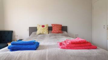 Una cama con edredón gris, dos almohadas y dos toallas dobladas.