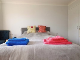 A bed with a grey duvet, two pillows, and two folded towels.