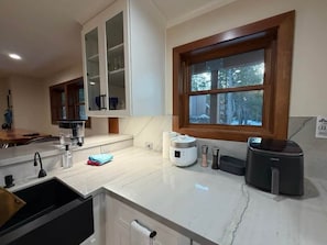 A kitchen with a built-in oven, a coffee maker, and a window with a view of trees. - Historic Stone Villa | Donner | Sauna | EV Charger (Soda Springs)