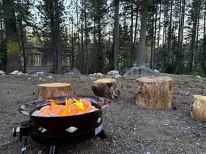 A campfire with logs and a metal fire pit in a forested area with trees and rocks. - Historic Stone Villa - Minutes to Sugar Bowl with Sauna and EV Charger (Soda Springs)