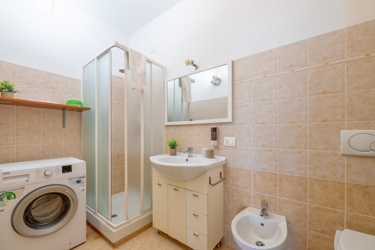 Une petite salle de bain équipée d’un lave-linge, d’une douche à parois de verre, d’un lavabo avec miroir et d’un bidet.