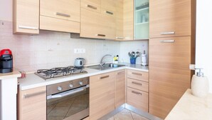 Een moderne keuken met lichte houten kastjes, een gasfornuis, een inbouwoven en een roestvrijstalen spoelbak.