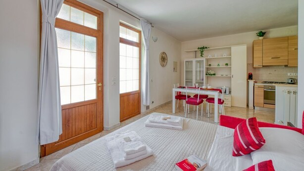 Een kamer met een bed, een eettafel met stoelen, een keukenhoek en een houten deur.