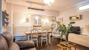 En moderne stue med sofa, spisebord, stole, fjernsyn og en lysekrone.