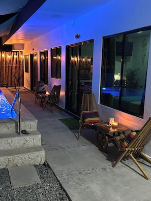 Et moderne udendørs opholdsområde med pool, stole og et bord med et lys.