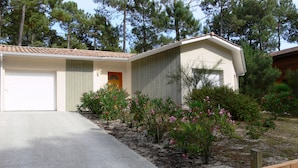 A single-story house with a garage, a front door, and a small garden with pink flowering plants. - Single-storey house under the pines in a peaceful setting between lake and ocean (CARCANS)