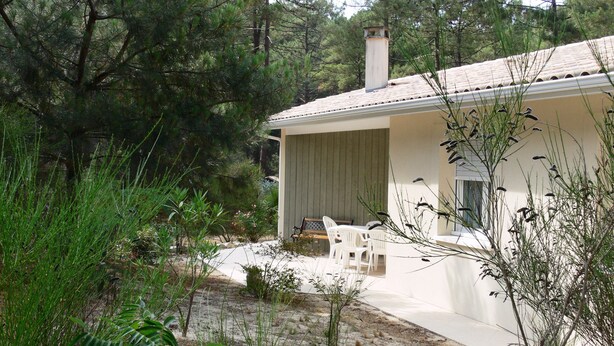 A house with a covered patio, outdoor seating, and a natural surrounding. - Single-storey house under the pines in a peaceful setting between lake and ocean (CARCANS)