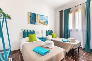 A hotel room with two beds, teal curtains, a painting of a coastal scene, and a drying rack. - Villa Carlotta by Perle di Puglia (Ostuni)