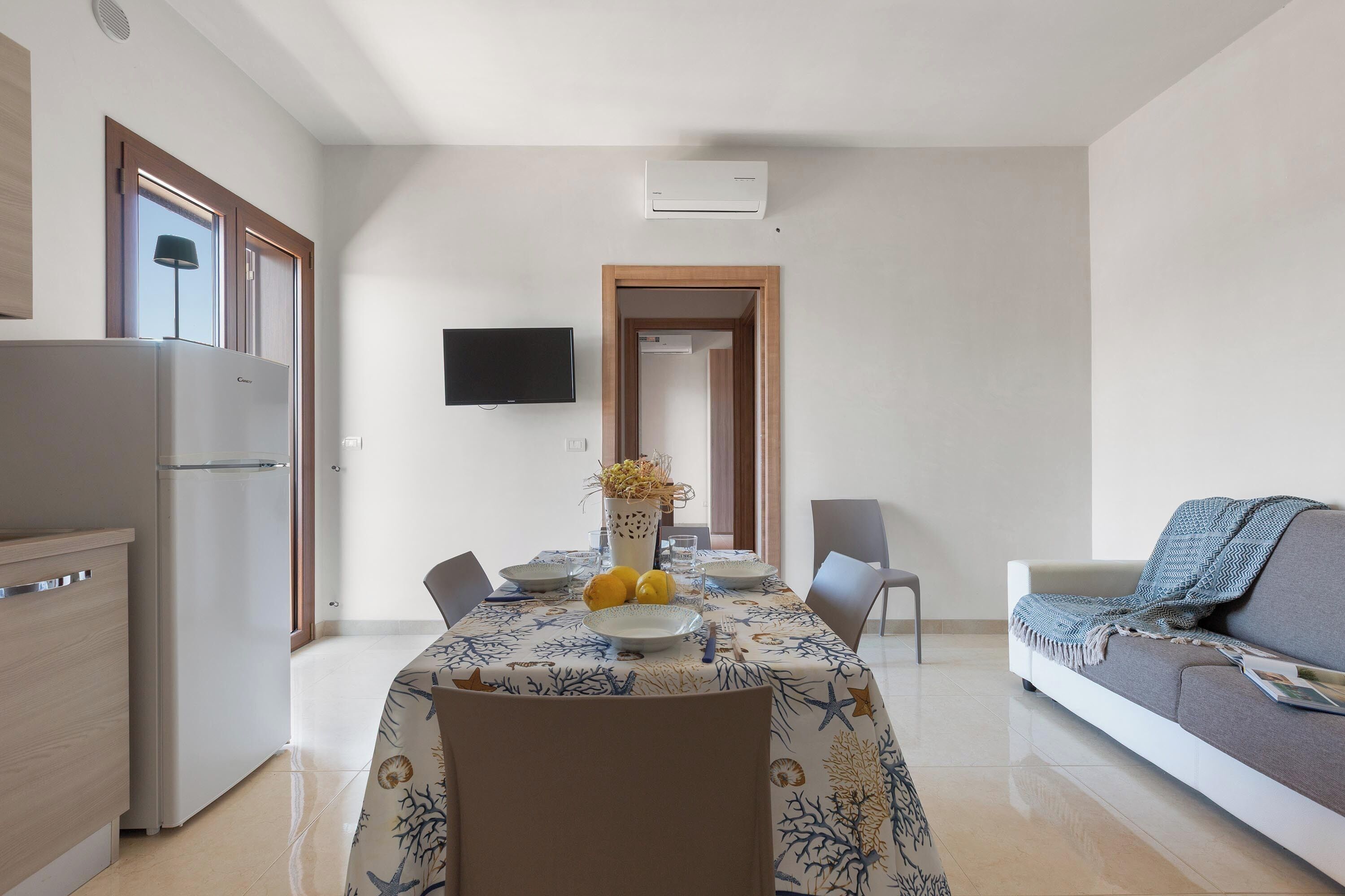 Une cuisine moderne équipée d’un réfrigérateur, d’une table à manger pour deux personnes et d’un téléviseur à écran plat fixé au mur.