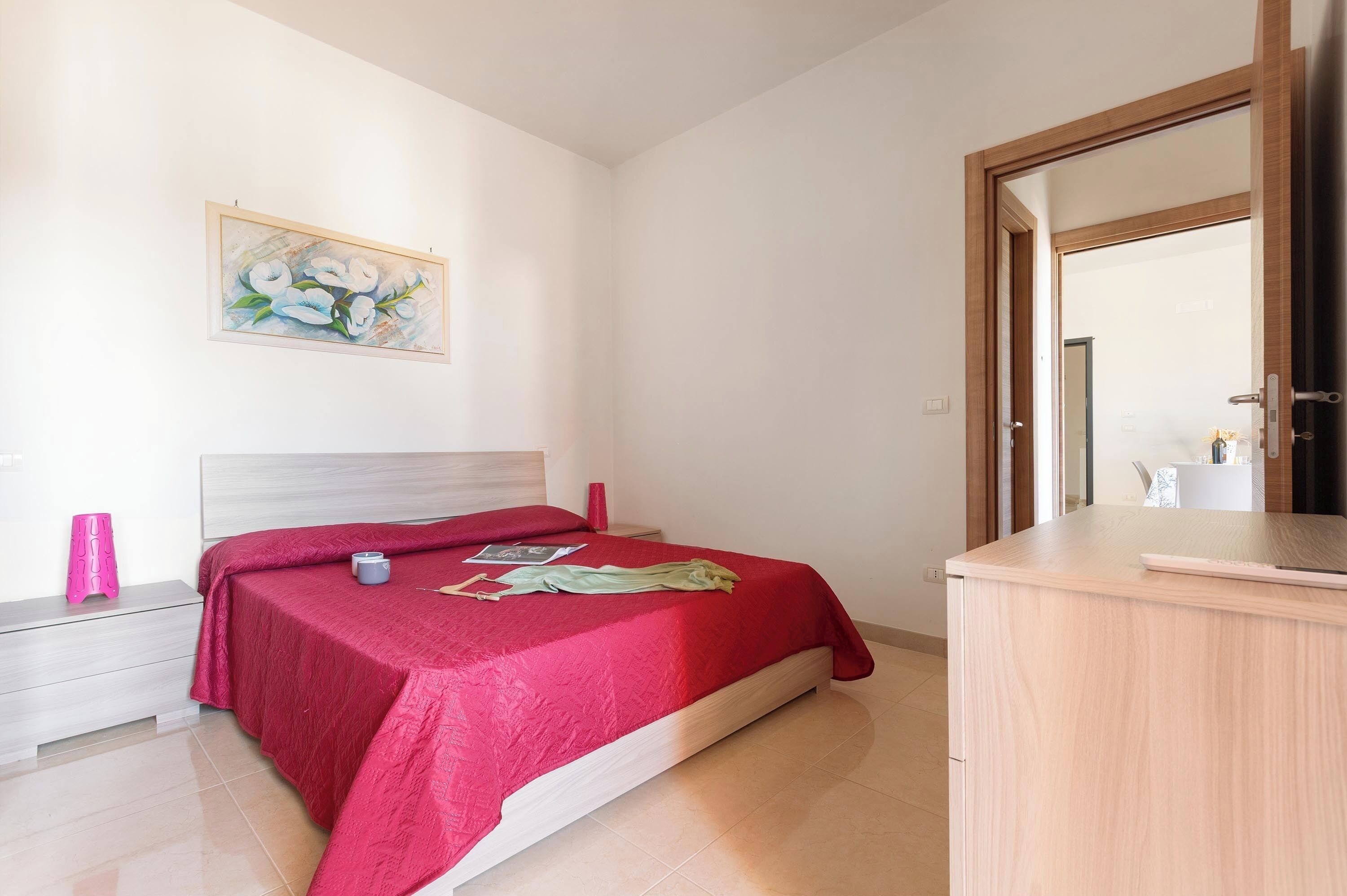 A bedroom with a bed, bedside table, nightstand, and a painting on the wall.