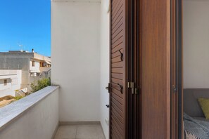 A balcony with a white wall, a wooden door, and a grey sofa with a green pillow. - Santoro Apartments - Trilo PP by BarbarHouse (Melendugno)