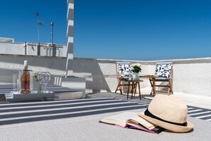 A rooftop terrace with a white wall, a table with a vase and flowers, two chairs, a hat, and an open book. - Infinito Luxury Rooftop by BarbarHouse (Monopoli)