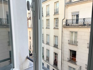 Vista desde una ventana de un edificio de varios pisos con balcones, un picaporte visible y un ventanal con una grieta.