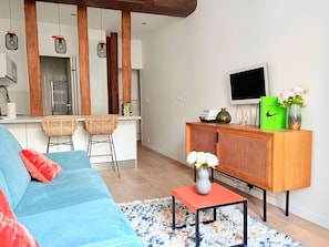A modern living room with a sofa, a small table with a vase, a TV, and a wooden cabinet with books and a vase. - Heart Marais Studio by Melvane (Paris)