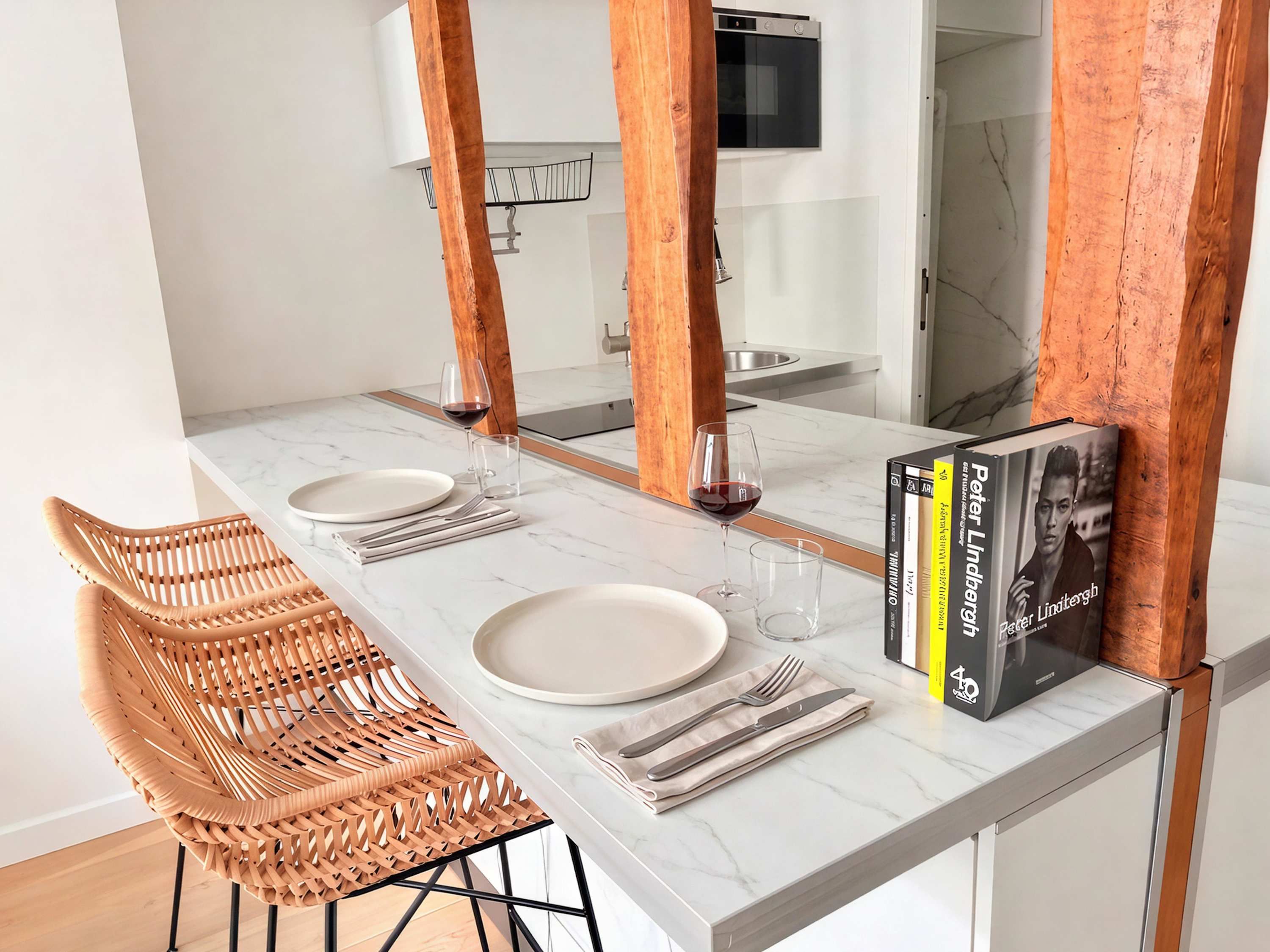 A dining area with a white marble table, two wicker chairs, and a book titled 'Peter Lindtberg'.