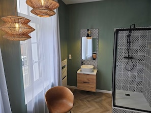 A bathroom with a wooden vanity, a large mirror, a white sink, and a shower with a patterned wall.