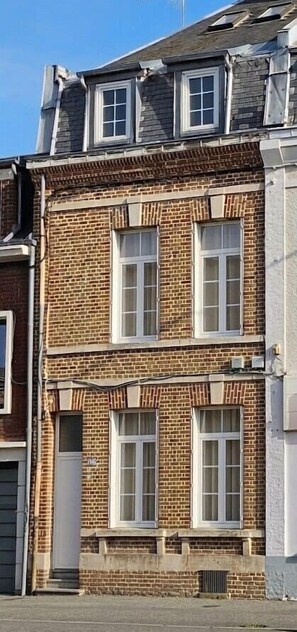 Un edificio in mattoni di due piani con finestre a cornice bianca e un portoncino piccolo.