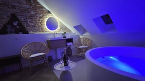 A modern bathroom with a bathtub, two wicker chairs, a round mirror, and a small sink.