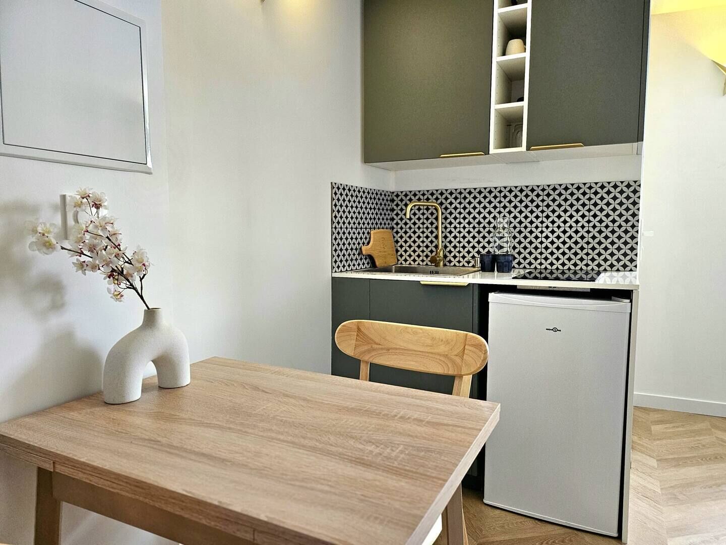 Una cucina compatta con un piccolo frigorifero, un lavandino e una sedia di legno.