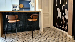A kitchen with a bar area, two bar stools, a microwave, and a coffee machine.