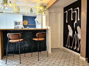 Una cocina con barra, dos taburetes de bar, microondas y cafetera.