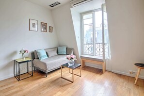 En moderne stue med sofa, sofabord, et lille bord med en vase, og et vindue med udsigt.