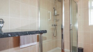 Un baño con cabina de ducha de vidrio, un perchero y un cubo de basura.