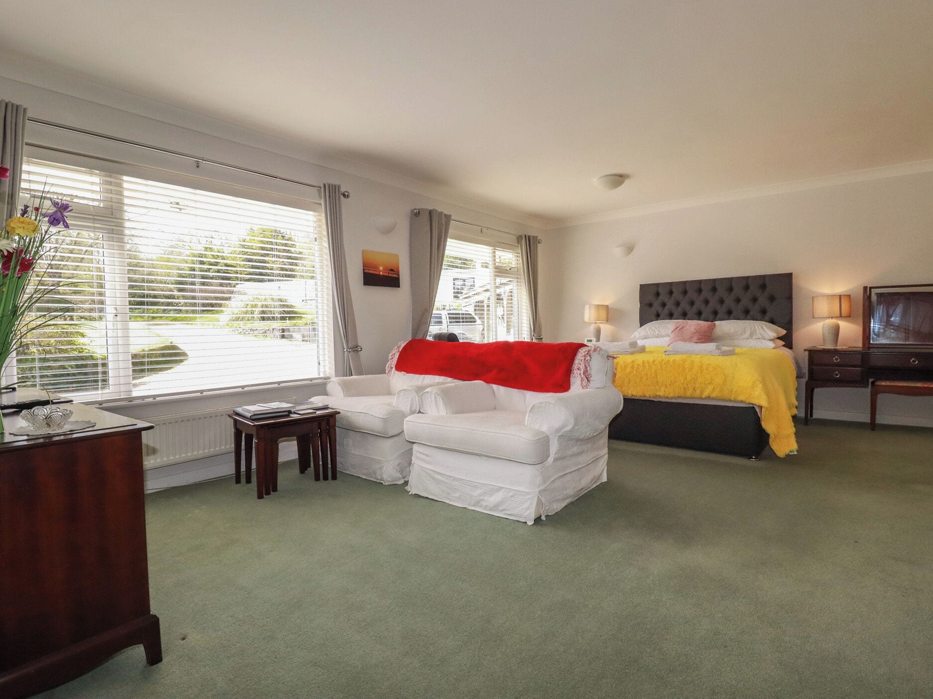 A hotel room with a bed, a sofa, a desk, and a window with blinds.