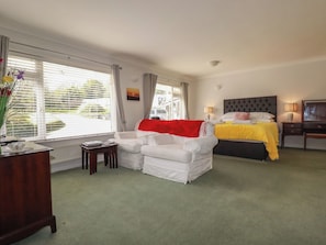 A hotel room with a bed, a sofa, a desk, and a window with blinds. - Tregoning Annexe (Lostwithiel)