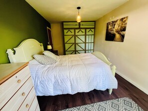 A bedroom with a bed, dresser, nightstand, lamp, and a painting on the wall.
