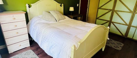 A bedroom with a bed, dresser, nightstand, lamp, and patterned rug.