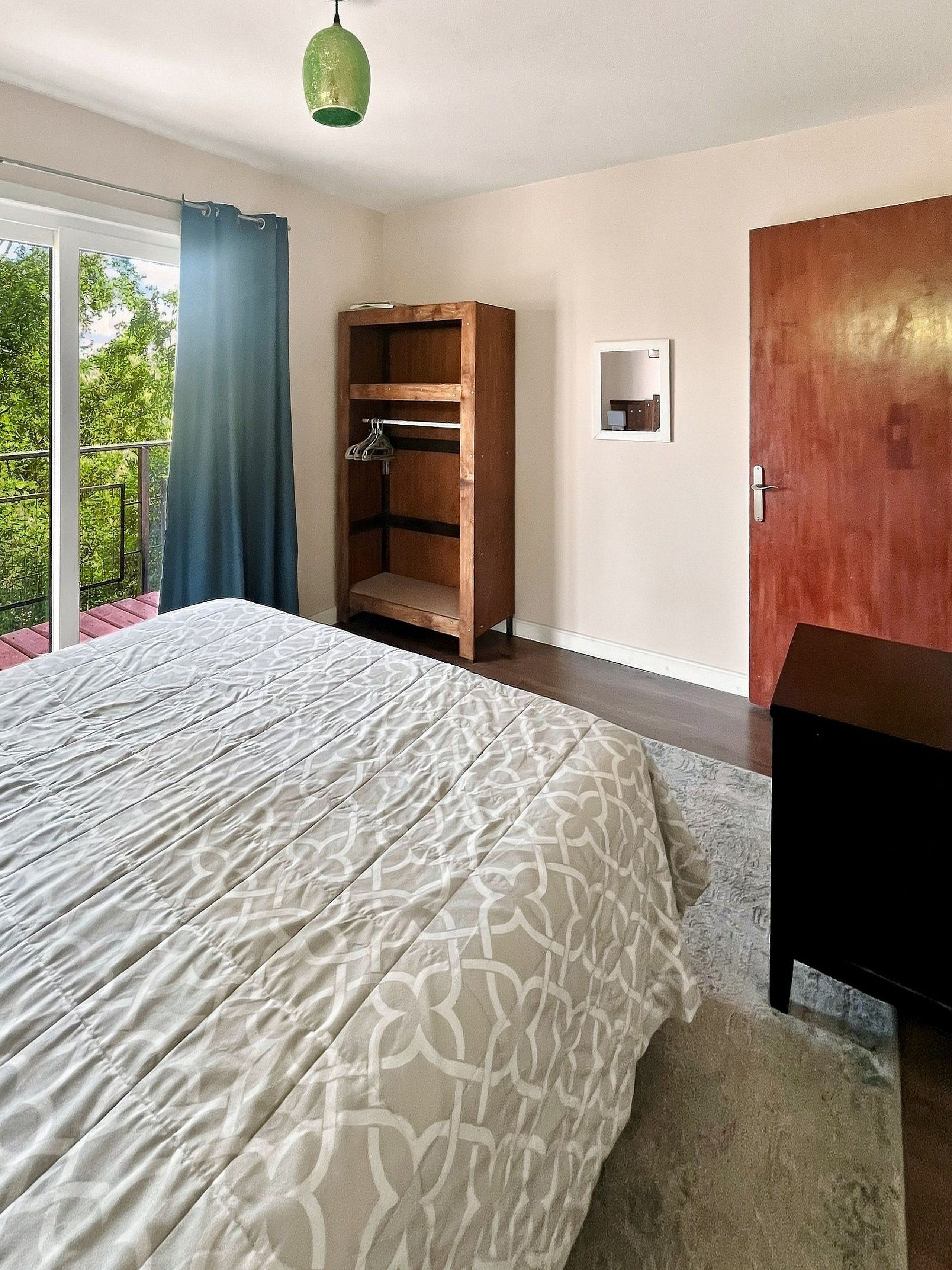 A bedroom with a large bed, a wooden wardrobe, and a small window.
