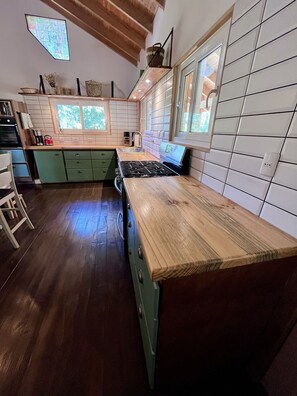 A kitchen with a wooden countertop, green cabinets, a stove, and a window. - Oceana Suites Lago Panguipulli (Panguipulli)