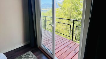 Una stanza con un'ampia porta-finestra scorrevole che si apre su un balcone con pavimento in legno e ringhiera metallica.