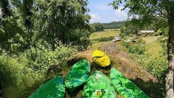 A row of kayaks on a grassy path with trees and a rural landscape in the background.