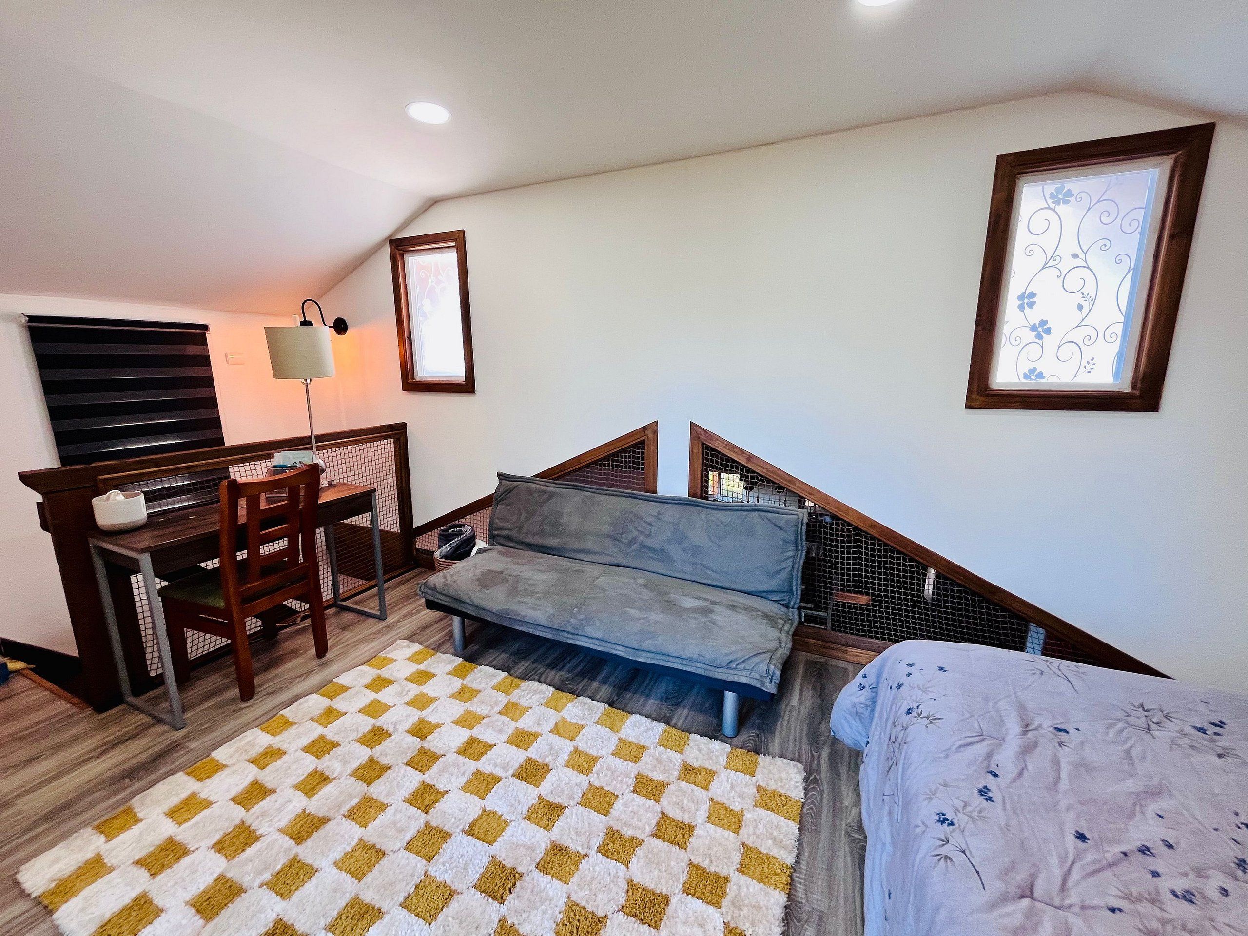 Quarto com cama, escrivaninha, cadeira, sofá, tapete estampado e escada.