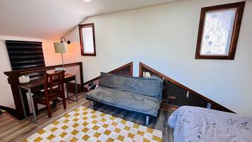 Quarto com cama, escrivaninha, cadeira, sofá, tapete estampado e escada.