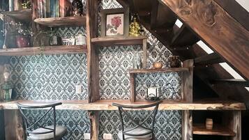 Um espaço de bar rústico com móveis de madeira, dois banquetas e uma estante cheia de livros e objetos decorativos.