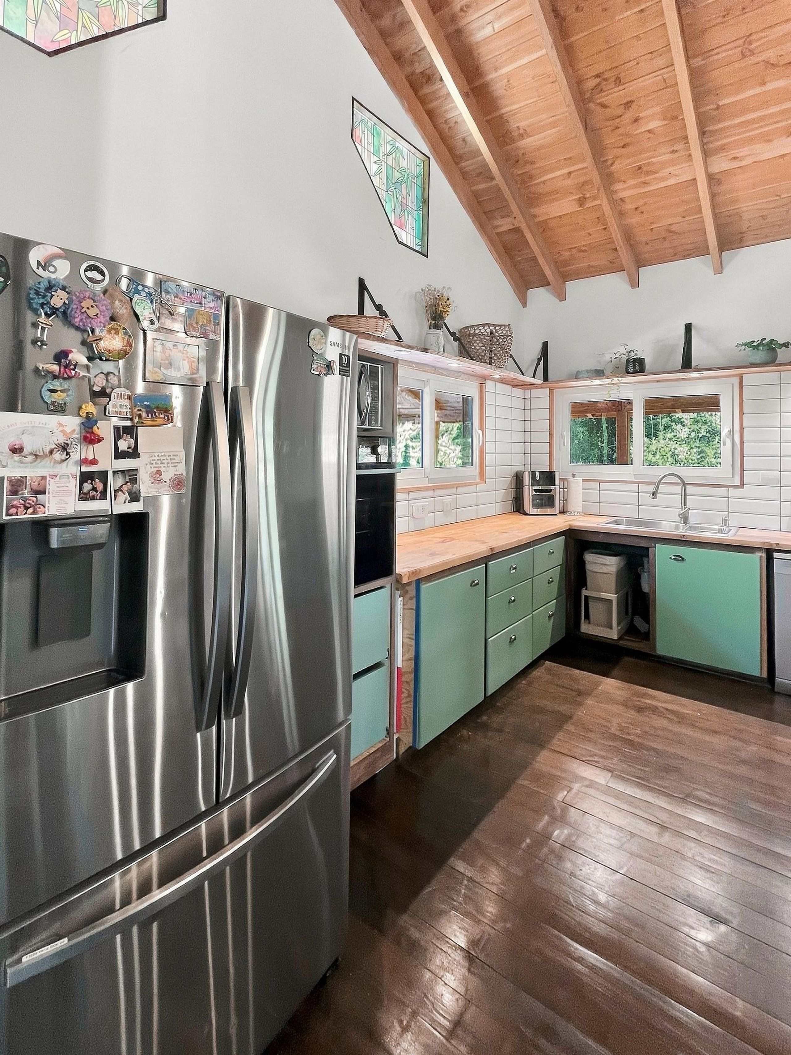 Una cocina con un refrigerador de acero inoxidable, techo de madera y armarios verdes.