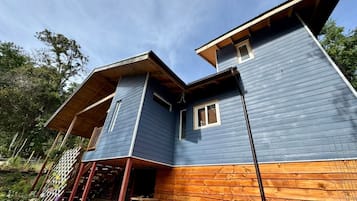 Une maison en bois à deux étages, dotée d’un porche et d’une petite dépendance attenante.