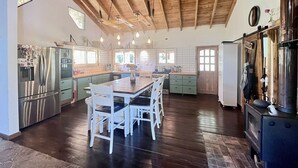 Una cocina amplia con techo de madera, una isla central con asientos, electrodomésticos de acero inoxidable y un gran ventanal que proporciona luz natural.