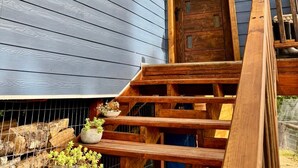 Una escalera de madera que conduce a una puerta azul oscuro, rodeada de barandillas de madera y macetas con plantas.