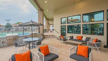 Un patio exterior con mobiliario, una parrilla y vista a una piscina.