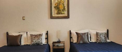 Una habitación con dos camas, una mesita de noche, un cuadro enmarcado en la pared y una lámpara en el techo.