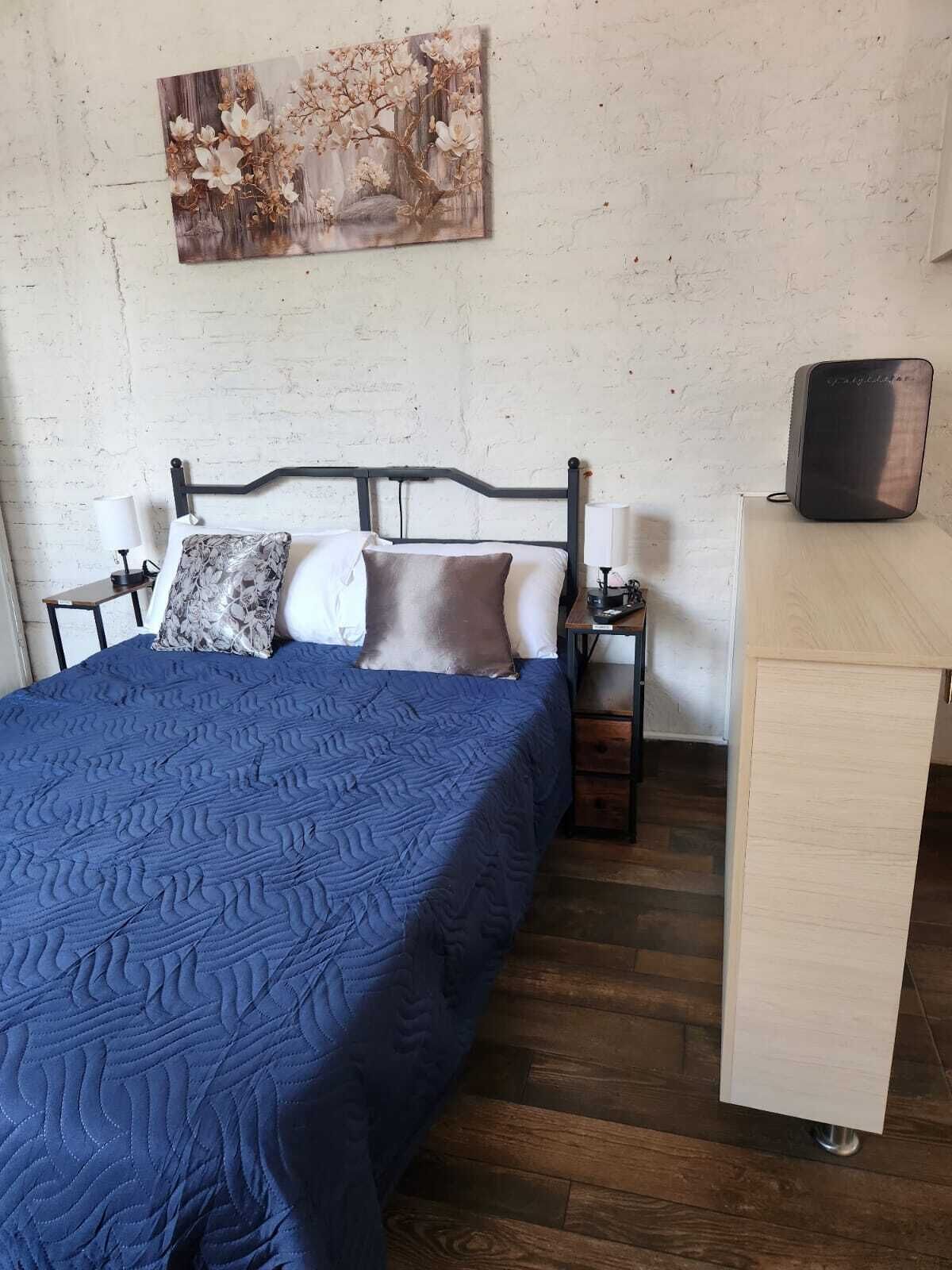 A bedroom with a bed, bedside tables, a desk, and a wall-mounted painting.