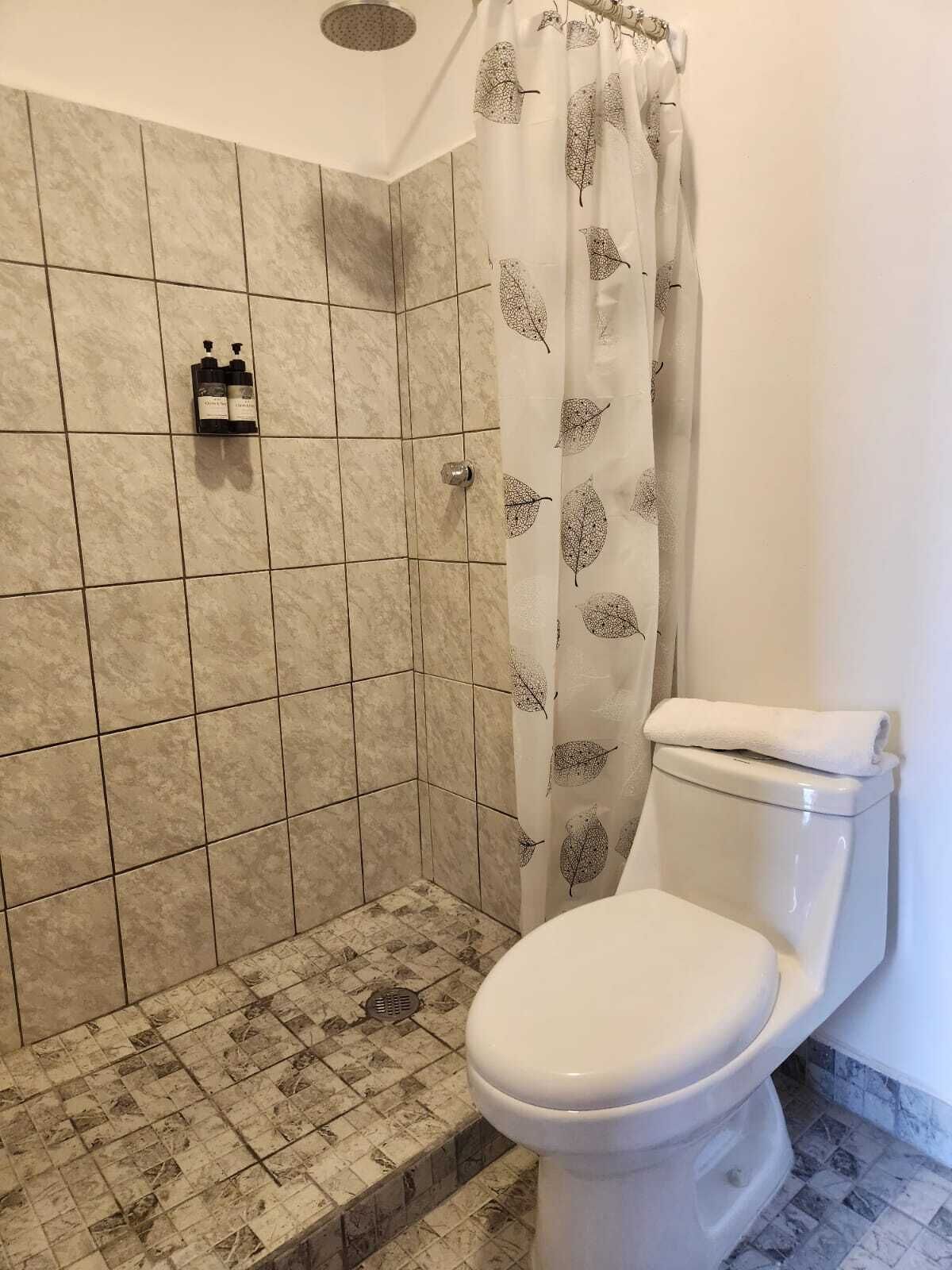 Egy fürdőszoba zuhanyzóval, WC-vel és törölközőtartóval.