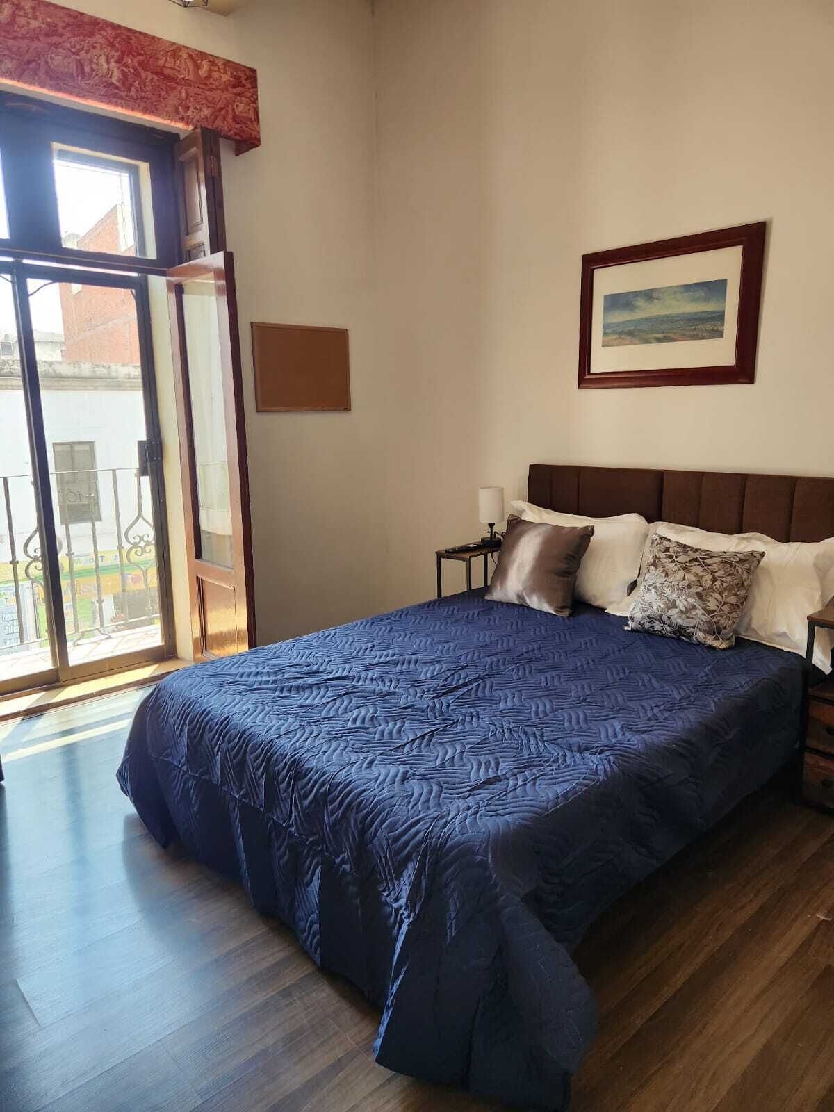 A bedroom with a large bed, a nightstand, a framed picture on the wall, and a sliding glass door leading to an outdoor area.