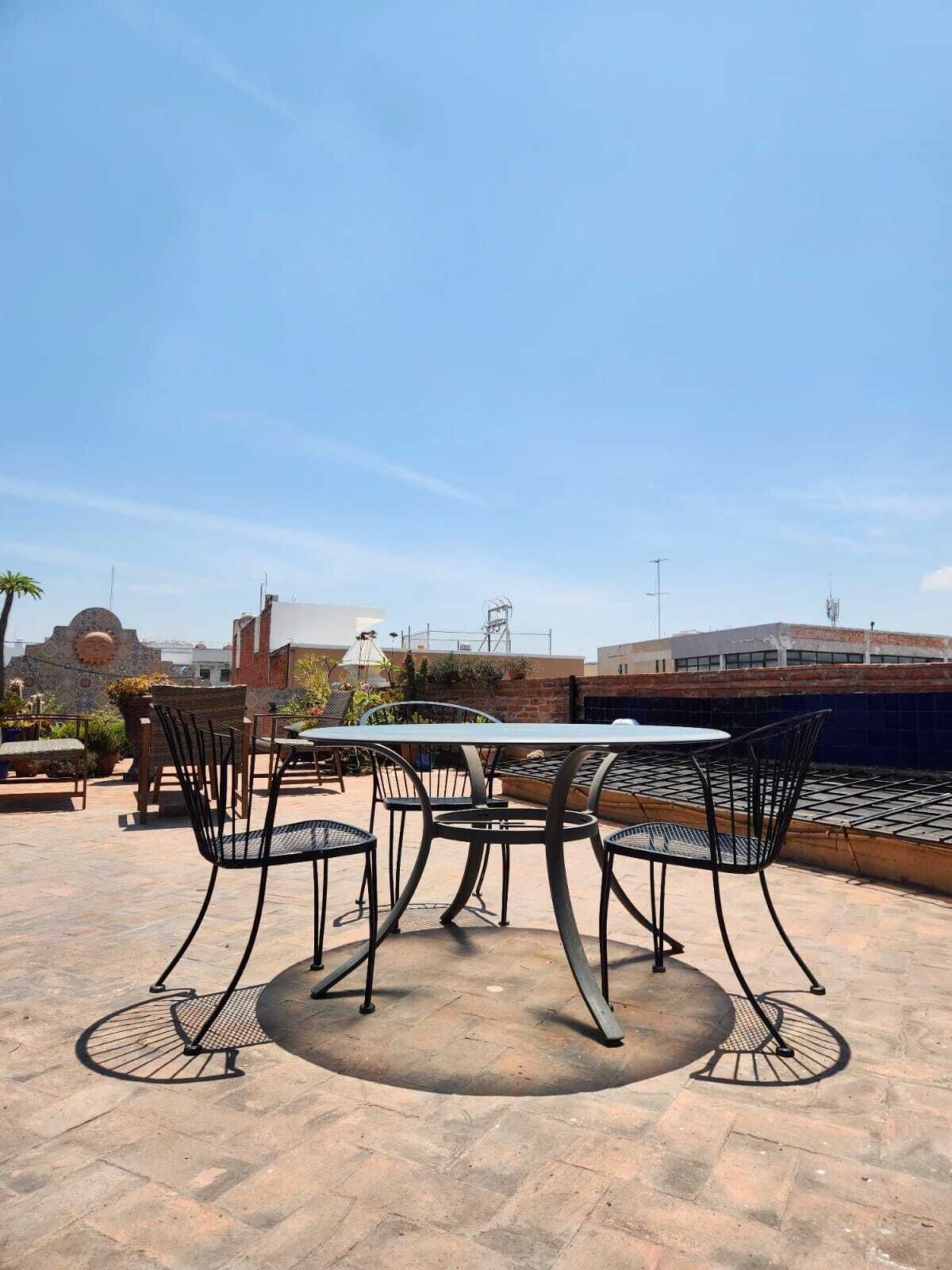An outdoor patio with a round table and chairs, a brick wall, and a clear blue sky.