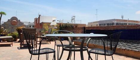 An outdoor patio with a round table and chairs, a brick wall, and a clear blue sky.