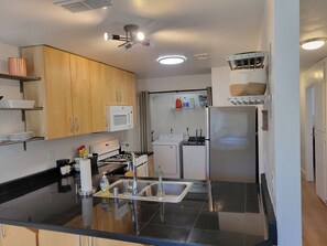 Eine moderne Küche mit schwarzem Arbeitsplatz, Edelstahlgeräten, Holzschränken und einem Deckenventilator.